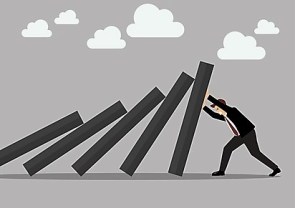 Businessman pushing hard against falling deck of domino tiles